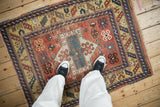 Close-up of antique Kazak border with navy and brick red serrated leaf motif on sand ground, with fringe.
