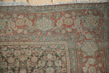 Senneh rug corner with worn cochineal red, dusty teal florals, and fringe.