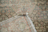 Antique distressed Senneh rug's folded corner, showing fringe, bare selvage, and muted floral motifs.