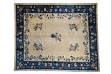 Antique Peking carpet with a beige open field, scattered blue and blush floral sprays, and a wide navy border.