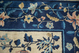 Articulated floral sprays in blush and sand on the cobalt and ivory borders of an antique Peking carpet.