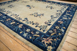 Angled view of an antique Peking carpet highlighting the navy blue border and beige open field.