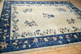 Antique Peking carpet viewed from an angle, featuring a beige open field and navy floral border.