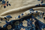 Antique Peking carpet folded, contrasting the navy floral border against the soft, sandy field.