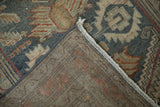 Folded corner of a distressed Malayer rug showing its low-pile texture and hand-knotted back.