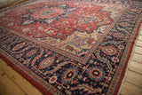 Angled corner view of a vintage Heriz rug showing the wide navy blue floral and serrated leaf border.
