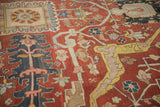 Angled detail of an antique Heriz carpet's elaborate arabesques in saffron yellow and dusty blue over a cherry red field.