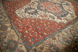 Angled view of Antique Karaja carpet showcasing copper red field with blue blossoms and beige border.