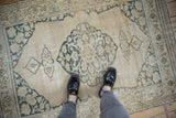 Distressed antique Doroksh rug corner detail, with dusty teal scrolling vines and muted palette.