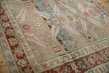 Angled view of a distressed Karaja carpet, showing the varied pile and red starburst vine border.