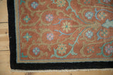 Corner of an antique Nichols rug showing its carved pile, floral vines, and black border.