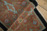 Dense wool pile of a rolled antique Nichols rug showing terracotta and powder blue scrolling vines.