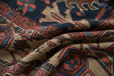 Folds of Gorevan carpet reveal geometric serrated palmettes in navy, blush, and beige.