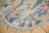 Close view of the round rug's beige fringe and hand-knotted Art Deco landscape pattern.