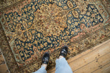 A view showing the scale and worn texture of an antique Malayer rug's floral medallion and navy field.