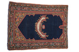 Antique Persian saddle cover rug with a navy field, central horn motif, and colorful geometric borders.