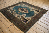 Angled view of a square Persian Bakshaish rug showing its blue shield medallion and beige field.