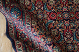 A soft wave in a vintage Sarouk rug reveals the rich texture of its red and navy floral pattern.