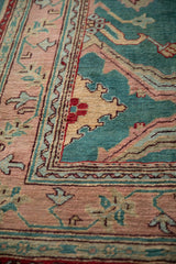 Hand-knotted Oushak rug detail: jade green field with scrolling vines and a dusty rose border.