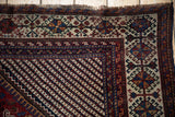Corner of an antique Qashqai carpet with a geometric ivory border and diagonal field pattern.