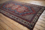 Full-length angled view of an antique Qashqai carpet with geometric medallions and intricate borders.