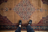 Overhead view of an antique Senneh rug's camel brown field with abrashes and intricate Herati medallion.