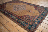 Angled view of an antique Persian Senneh rug showing its abrashed camel field and detailed Herati medallion.