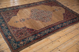 Perspective view of an antique Senneh rug, detailing the camel field, central medallion, and intricate spandrels.