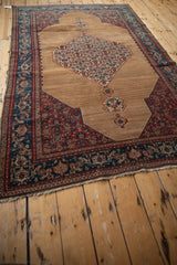 Antique Senneh rug from a high angle, highlighting the medallion and spandrels on the camel field.