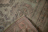 Folded corner of Vintage Oushak rug, revealing dusty rose, green pile with scrolled tendrils.