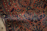 Rolled edge of a vintage Sarouk rug runner, dusty rose pile, navy border with floral motifs.