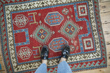 Antique Kazak rug underfoot, showing the scale of its geometric pattern and gem-tone colors.