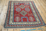 An antique Kazak rug laid at an angle, displaying its vibrant red field and complex geometric borders.
