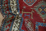 The reciprocating wave border and low wool pile of an antique hand-knotted Kazak rug.
