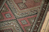 Serrated geometric patterns and pawn motif border in aubergine, sage, and ivory tones.