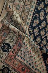 Folded antique Malayer rug detail with a dark navy field of repeating botehs and an ivory patterned border.