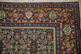 Corner of a vintage Persian Senneh rug showing the Samovar Turtle border and navy Herati field.