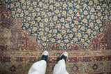 Antique Kermanshah carpet: millefleur blossoms on cobalt blue field, scrolling dusty aubergine border, even wear.