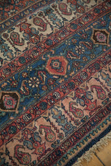 A detailed view of the vintage carpet's boteh and shrub border motifs in red and blue.