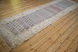 Angled perspective of a distressed Malayer runner showing its faded boteh pattern and ivory floral border.