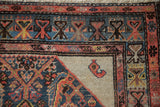 Corner of an antique Hamadan showing the geometric border, worn ivory spandrel, and boteh motif.