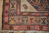 Corner detail of an antique Hamadan rug showing a geometric border, a singular boteh, and time-softened wool pile.