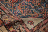 The sand-colored corner spandrel and singular boteh motif of an antique Persian Hamadan rug.