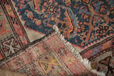 Folded corner of an antique Hamadan rug showing the reverse weave, front pile, and fringe.