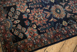 Close-up of serrated leaves and palmettes in blush and teal on a navy blue vintage Lilihan rug.
