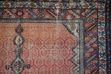 Corner detail of an antique Hamadan rug with a serrated leaf border and a dusty red lattice field.