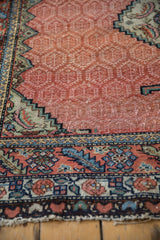 Angled view of an antique Persian rug's worn pile, showing the serrated border and geometric field.