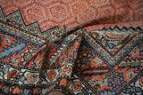 The intricate, serrated border and low-pile ruby field of a draped antique Hamadan rug.