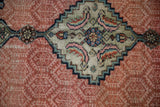 Close-up on a Samovar stylized medallion with dusty sage green and pink on a worn ruby red field.