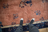 Antique Peking rug's aged copper field texture, blue floral sprays, and navy border, with feet.